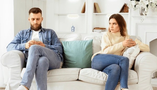 couple assis dos à dos dans un salon sombre, symbolisant le silence et la distance émotionnelle caractéristiques d'un couple bloqué dans sa communication