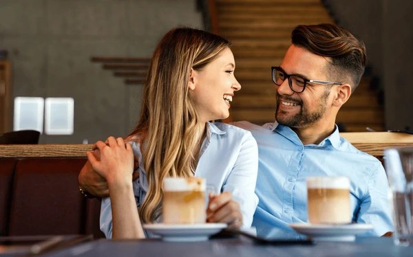 couple assis face à face dans un café chaleureux, échangeant avec attention et bienveillance, symbolisant le retour du dialogue sincère dans une relation en voie de guérison